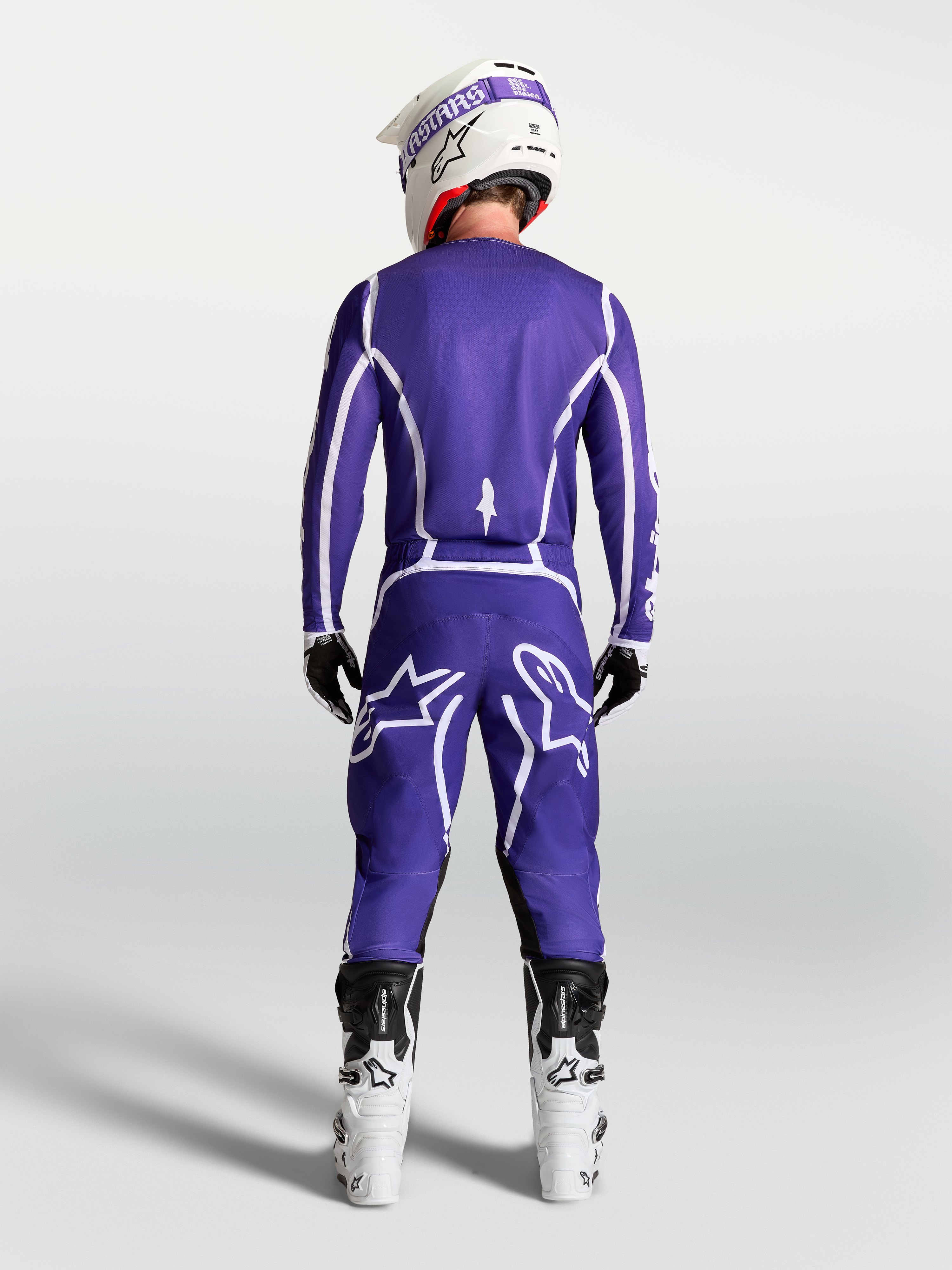 Alpinestars Maglia Fluid Apex V2, maglia da motocross blu e bianca, vista posteriore su pilota con pantaloni e stivali bianchi.