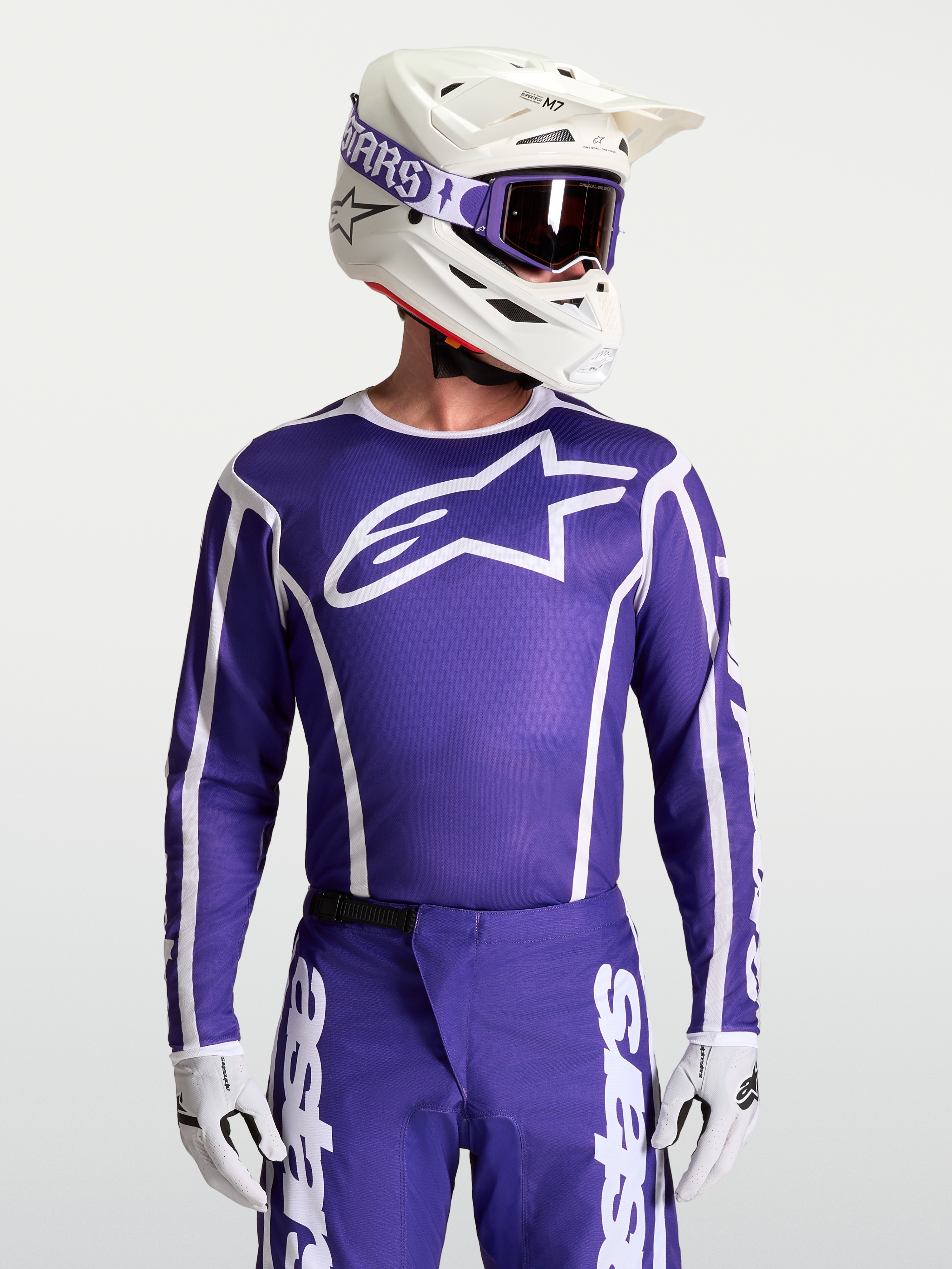 Alpinestars Maglia Fluid Apex V2, maglia da motocross blu e bianca, vestibilità atletica ergonomica, tessuto traspirante, indossata da un pilota con casco e protezioni.