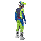 Pilota di motocross visto da dietro con maglia Alpinestars Racer Hoen 2024 in Giallo Fluo e Blu Night Navy, pantaloni da motocross abbinati e stivali bianchi, mostra il design posteriore con loghi rossi, completo coordinato per gare off-road professionali
