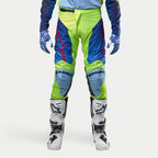 Alpinestars 2024 Racer Hoen Pants, pantaloni da motocross, Giallo Fluo e Blu Night Navy, indossati con stivali da motocross bianchi e neri e guanti blu, con loghi rossi vivaci, pannelli azzurri sulle ginocchia e un design ergonomico sportivo per la guida fuoristrada