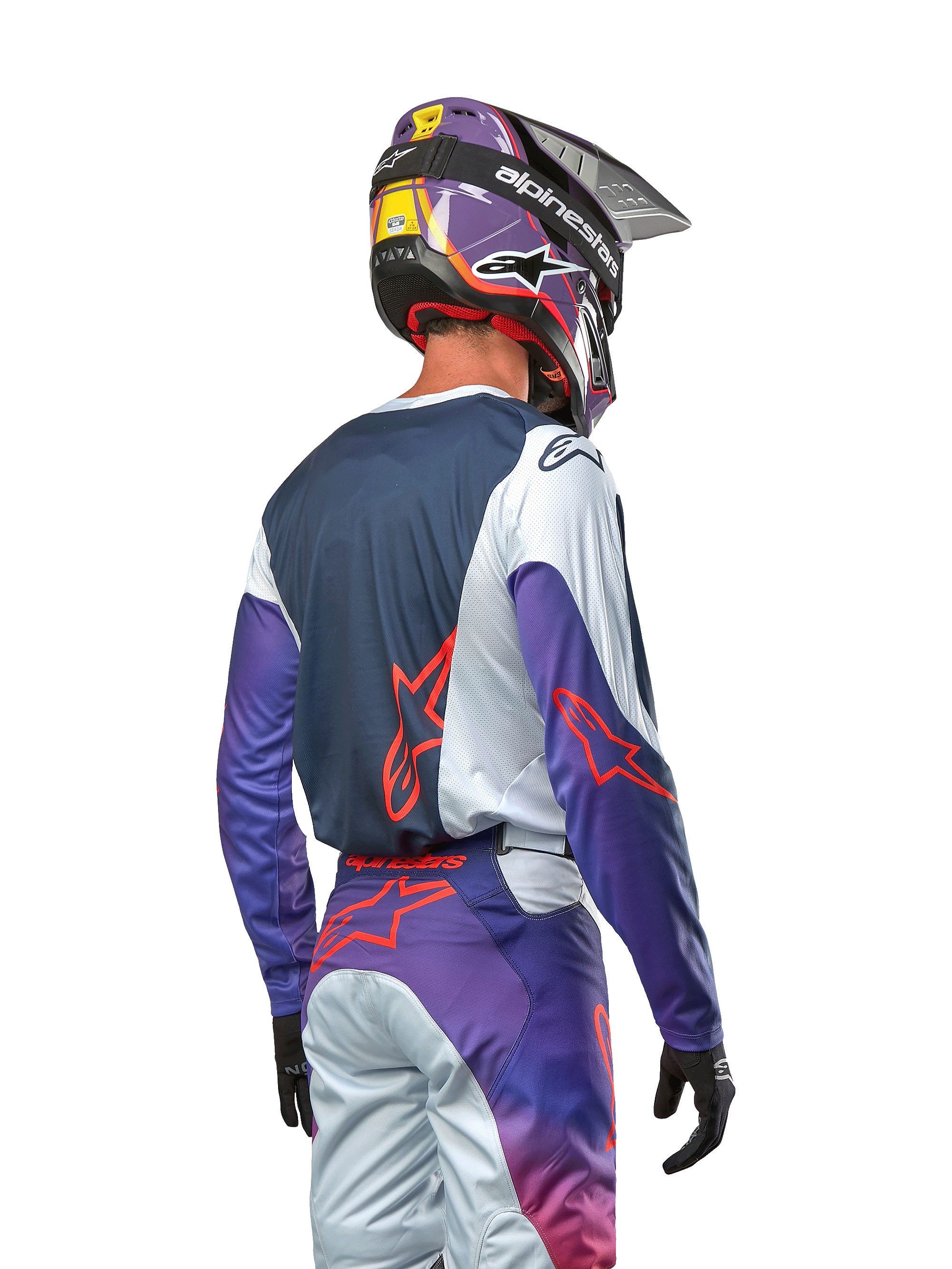 Pilota di motocross visto di spalle con indosso la maglia Alpinestars Racer Hoen 2024, pannello posteriore blu navy con spalle grigio chiaro e maniche viola, loghi Alpinestars arancione acceso, pantaloni coordinati viola e grigi e casco viola, kit da gara off-road completo