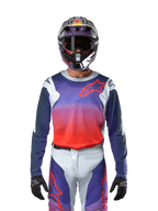 Alpinestars Racer Hoen Jersey 2024, maglia da motocross in grigio chiaro, arancione acceso e nero, indossata da un pilota con equipaggiamento coordinato, caratterizzata da una vivace sfumatura di colore e dal logo a stella Alpinestars sul petto, progettata per prestazioni fuoristrada