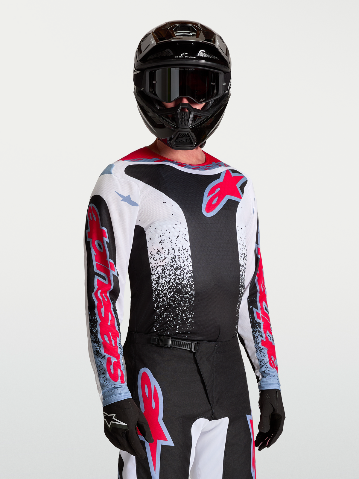 Alpinestars Maglia Fluid Drag, maglia da motocross da uomo, nera e bianca con accenti rossi e blu, in tessuto leggero e traspirante, indossata da un modello con casco e guanti coordinati