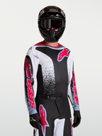 Alpinestars Maglia Fluid Drag, maglia da motocross da uomo, nera e bianca con accenti rossi e blu, in tessuto leggero e traspirante, indossata da un modello con casco e guanti coordinati