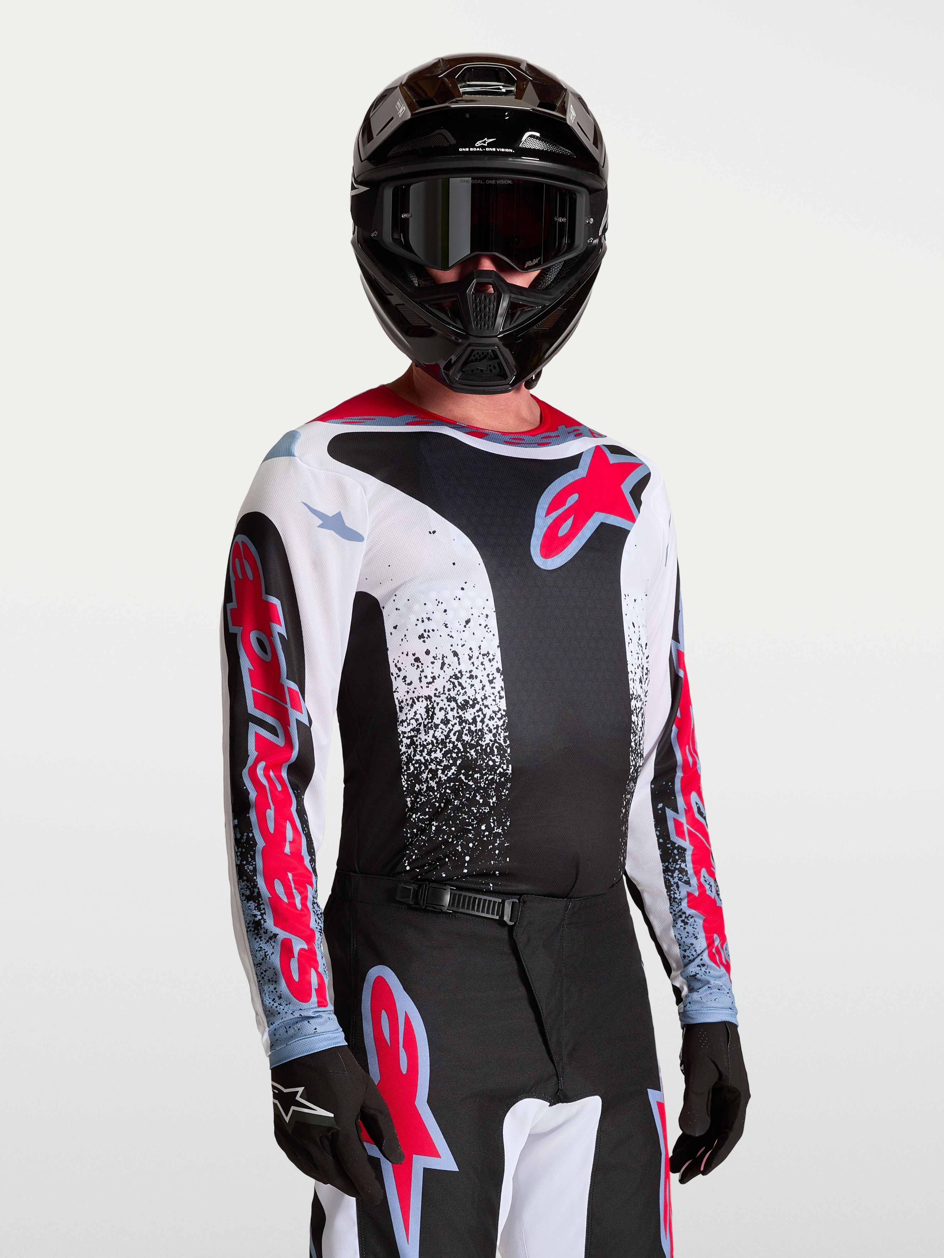 Alpinestars Maglia Fluid Drag, maglia da motocross da uomo, nera e bianca con accenti rossi e blu, in tessuto leggero e traspirante, indossata da un modello con casco e guanti coordinati