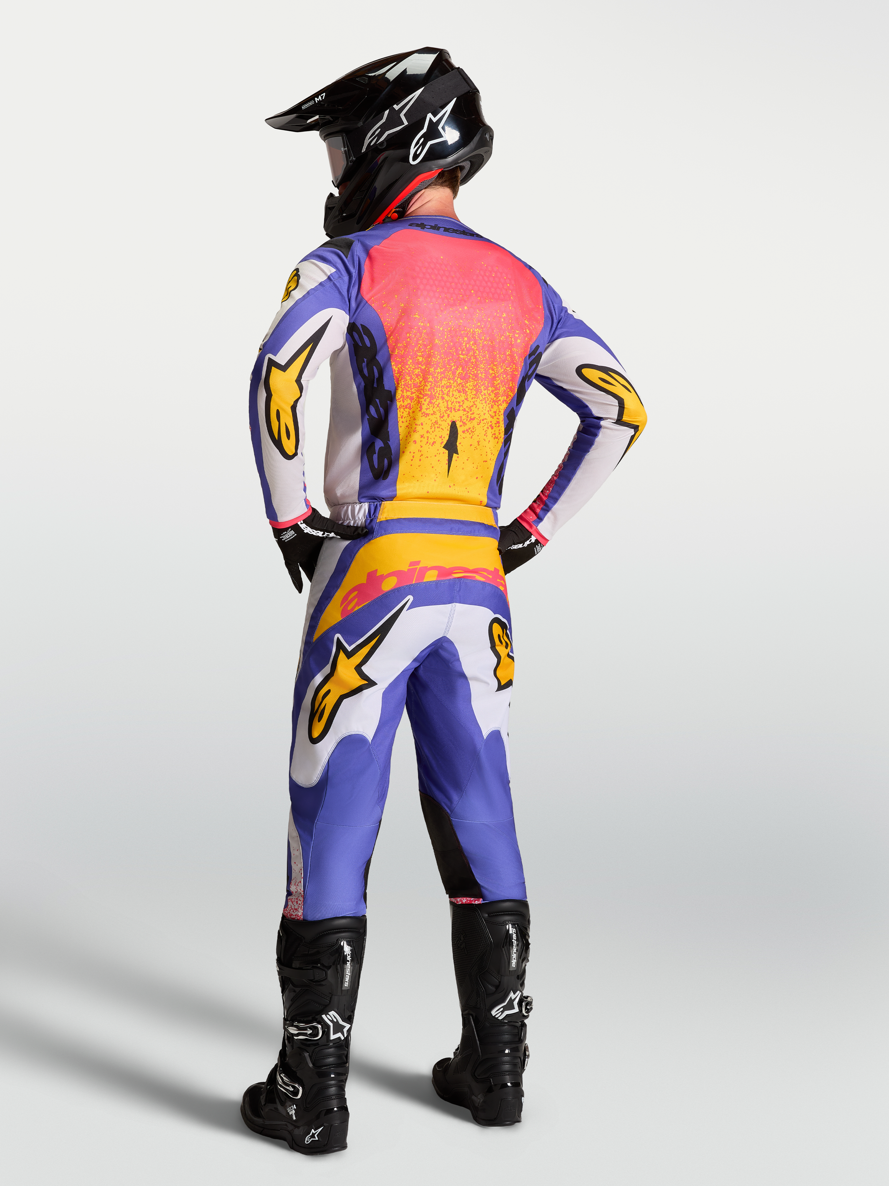 Alpinestars Maglia Fluid Drag, maglia da motocross lilla e blu con dettagli oro, vista posteriore su pilota