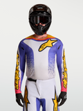 Alpinestars Maglia Fluid Drag, maglia da motocross da uomo, blu e oro, in tessuto leggero traspirante, indossata da un modello con casco e guanti, ideale per sessioni off-road