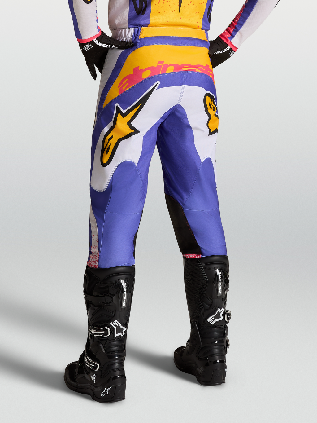Alpinestars Pantaloni Fluid Drag, pantaloni da motocross da uomo, blu e oro, con rinforzo posteriore, indossati con stivali neri, design pre-curvato per prestazioni off-road.