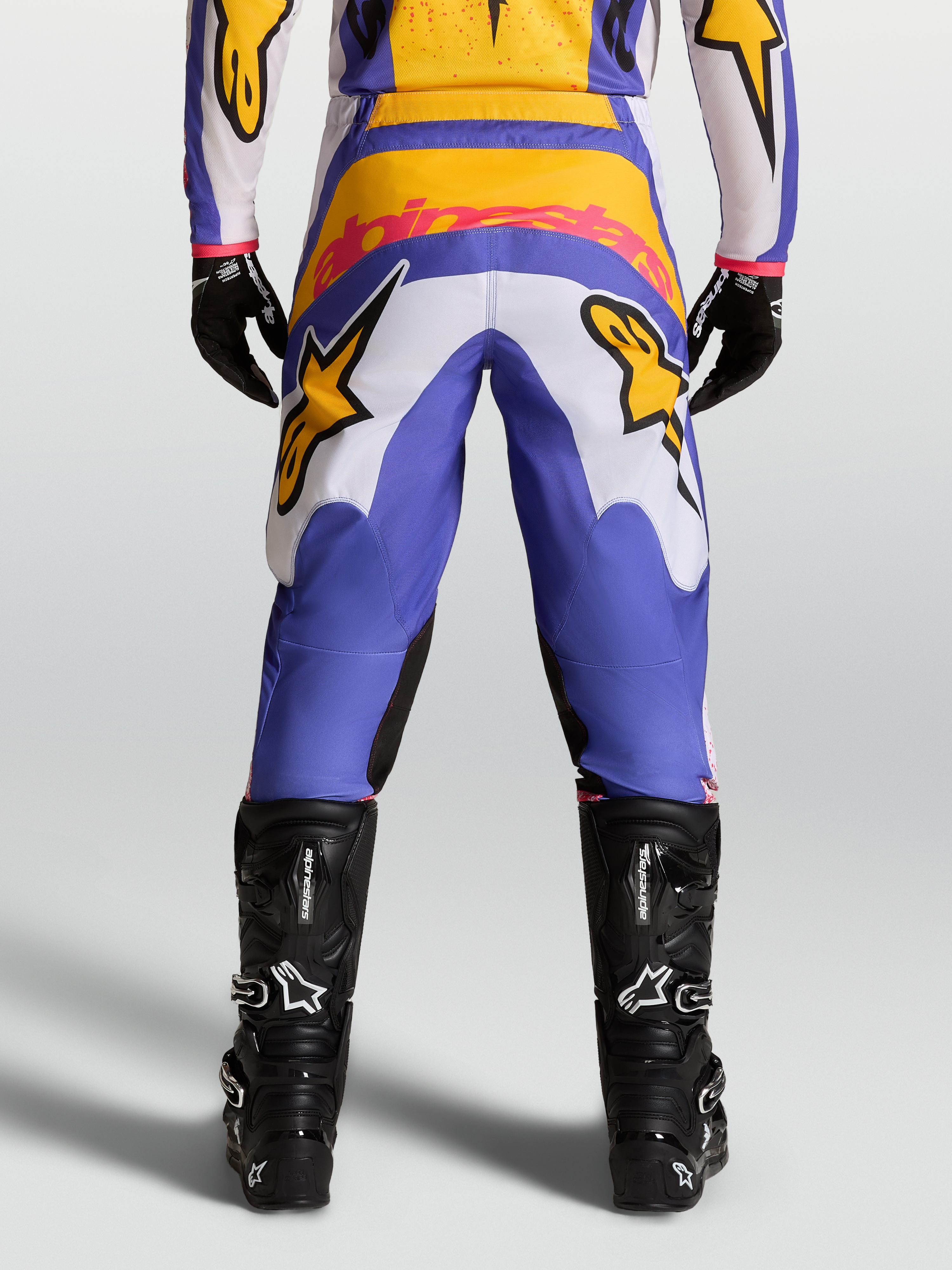 Alpinestars Pantaloni Fluid Drag, pantaloni da motocross blu e oro, vista posteriore, con pannelli elasticizzati e seduta rinforzata, abbinati a stivali tecnici neri