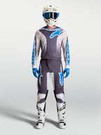 Maglia Alpinestars Fluid Drag grigia e blu, kit da motocross con casco e stivali racing bianchi coordinati.
