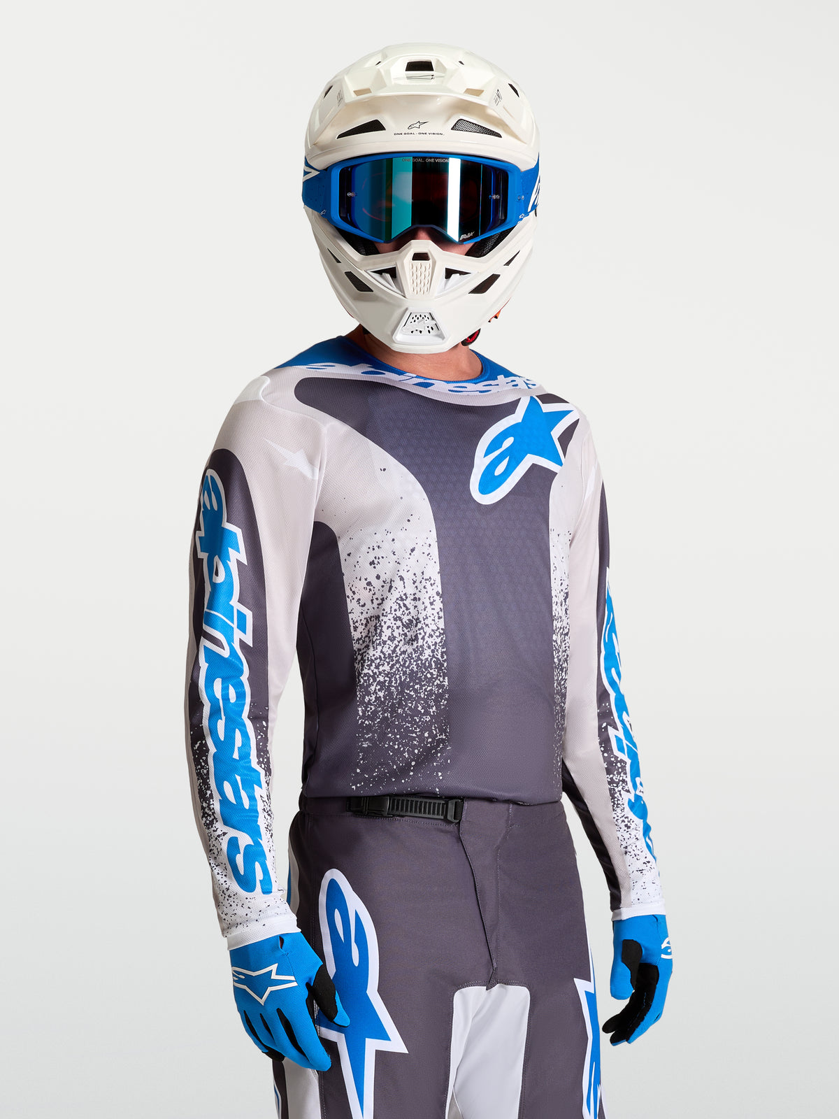 Alpinestars Maglia Fluid Drag, maglia da motocross fuoristrada per uomo, grigia e blu, indossata con casco bianco e guanti, tessuto tecnico traspirante