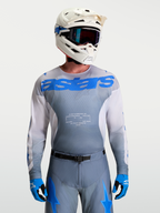 Alpinestars Maglia Racer Amber, maglia motocross da uomo, grigio fumo e blu UCLA, con casco e maschere bianche.