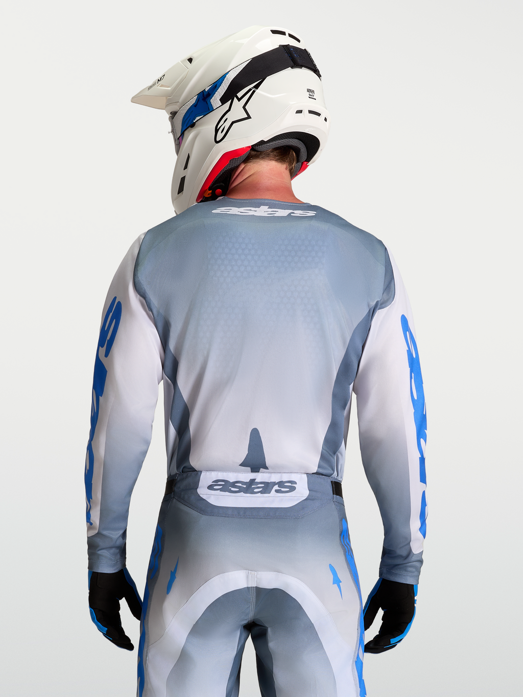Alpinestars Maglia Racer Amber, maglia da motocross grigio e bianco, vista posteriore su modello con casco bianco, in poliestere traspirante.