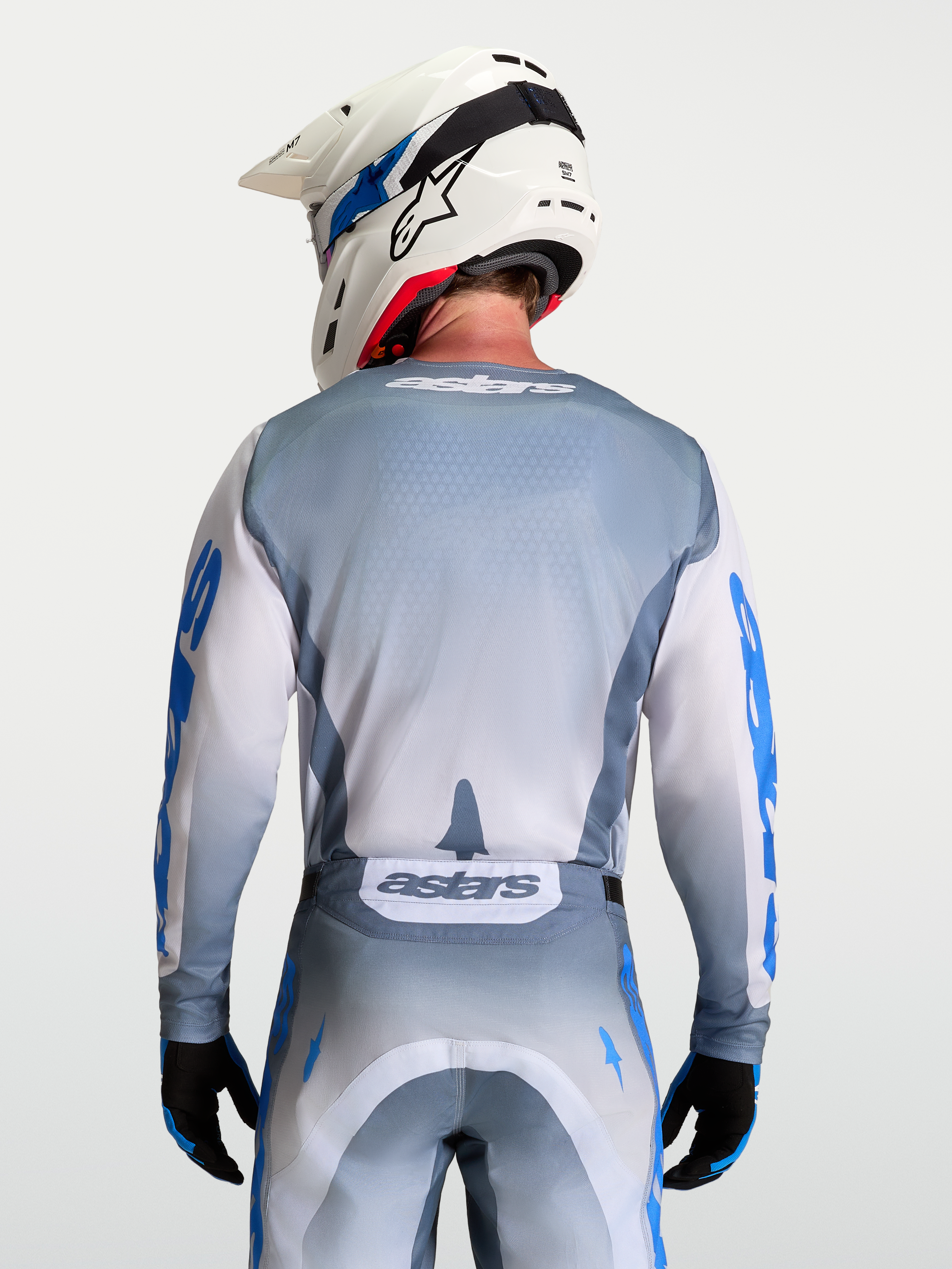 Alpinestars Maglia Racer Amber, maglia da motocross grigio e bianco, vista posteriore su modello con casco bianco, in poliestere traspirante.