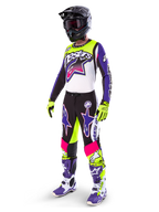 Pilota di motocross che indossa l'abbigliamento Alpinestars Limited Edition Supertech Dirt Studios®, schema colori bianco, viola e giallo fluo, pantaloni neri con grandi loghi a stella viola e rosa, guanti giallo neon, stivali da gara viola e bianchi, casco nero, kit professionale completo per prestazioni off-road