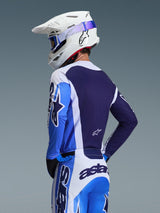 Pilota di motocross che indossa la maglia Alpinestars 2026 Racer Air Portl in blu Ucla e bianco, vista posteriore che evidenzia il pannello posteriore in mesh traspirante blu navy, abbinata a pantaloni coordinati e un casco bianco Alpinestars con occhiali blu, set di abbigliamento da motocross coordinato.