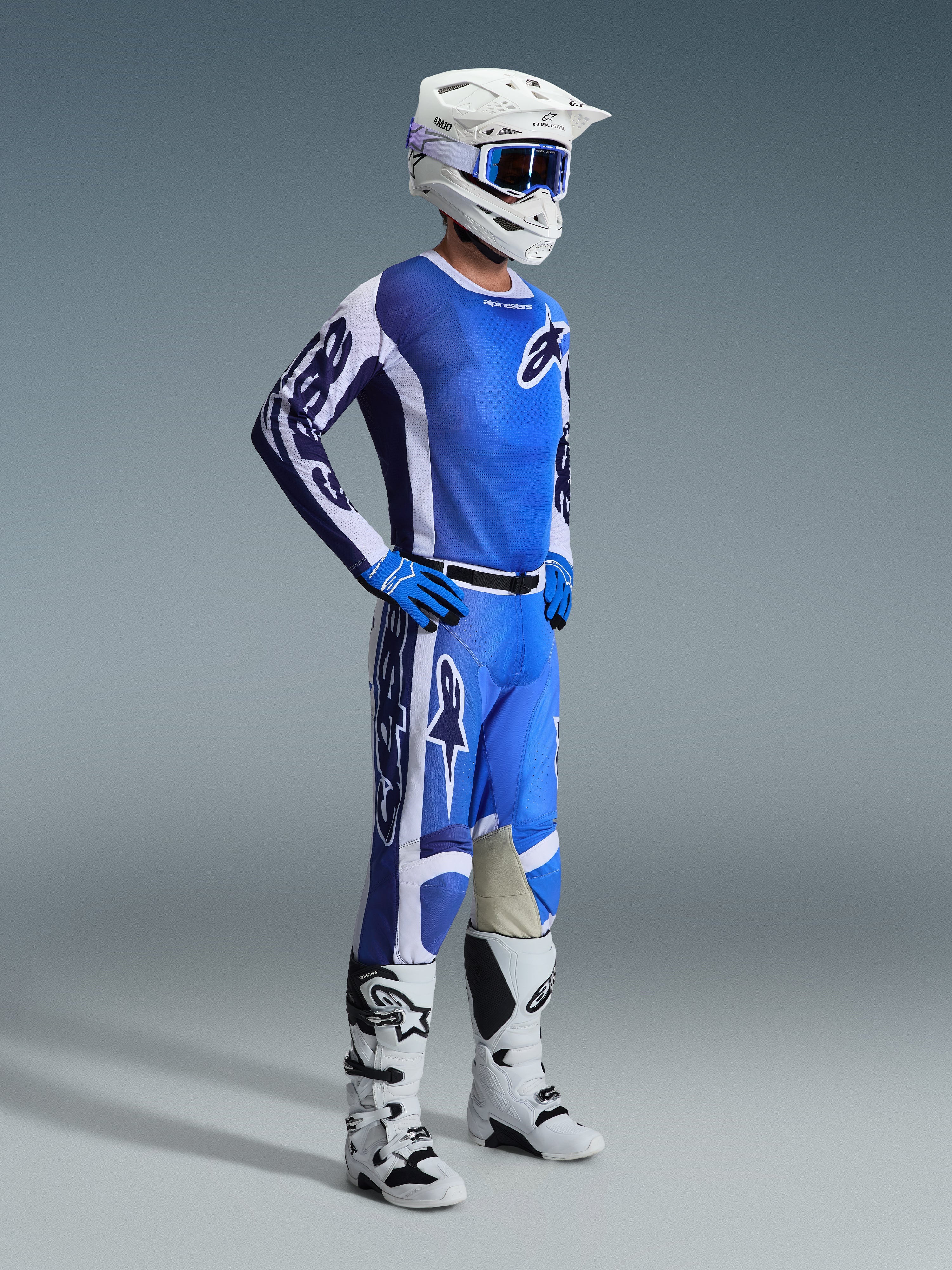 Alpinestars 2026 Racer Air Portl Gear Set, pilota di motocross che indossa un abbigliamento da gara completo ventilato, maglia blu e bianca con pantaloni abbinati, casco bianco con occhiali blu, guanti blu, stivali bianchi e neri, outfit ad alte prestazioni per la guida fuoristrada