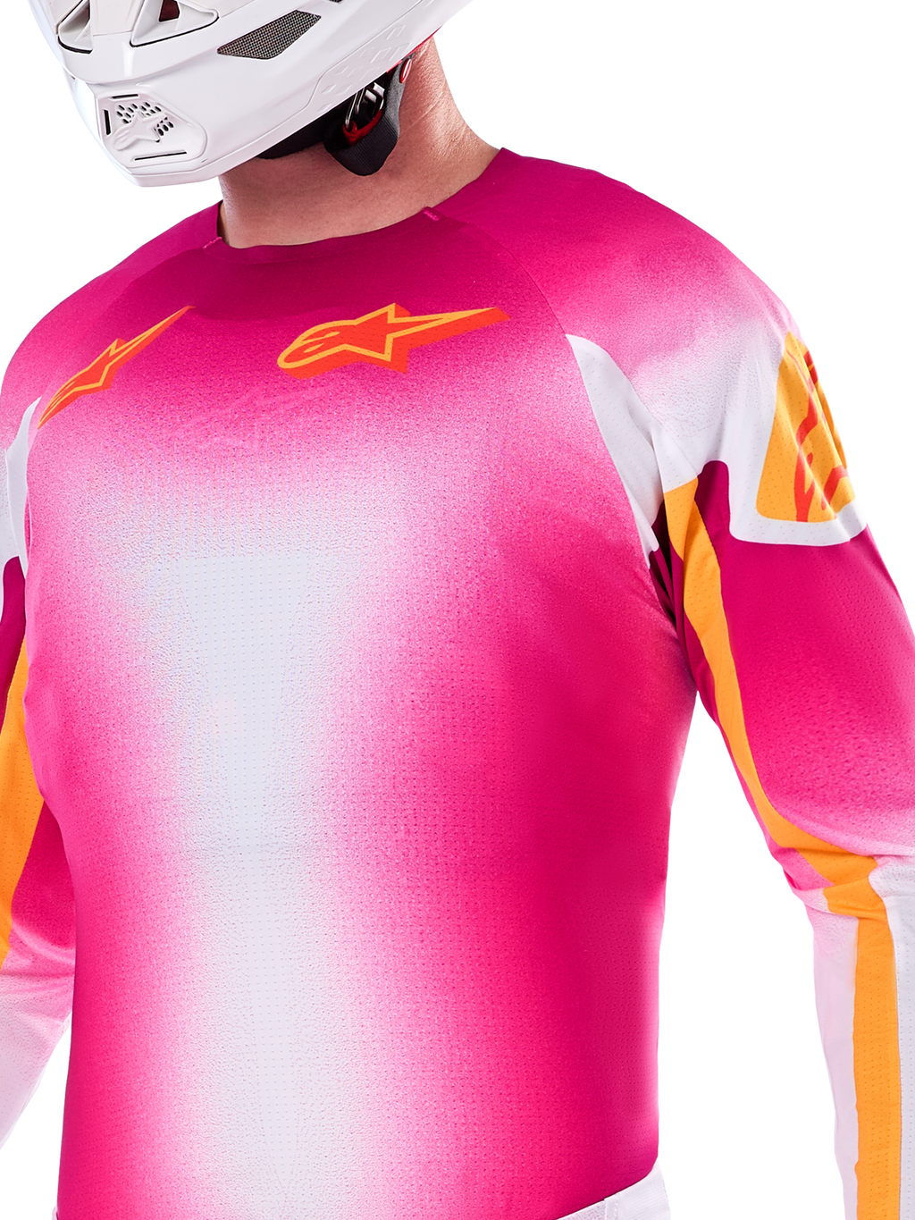 Alpinestars Limited Edition Supertech AFD MIG Jersey, maglia da motocross con sfumatura rosa fluo e bianco, loghi Astars e accenti sulle maniche arancioni, indossata da un pilota con casco bianco, vestibilità atletica da gara