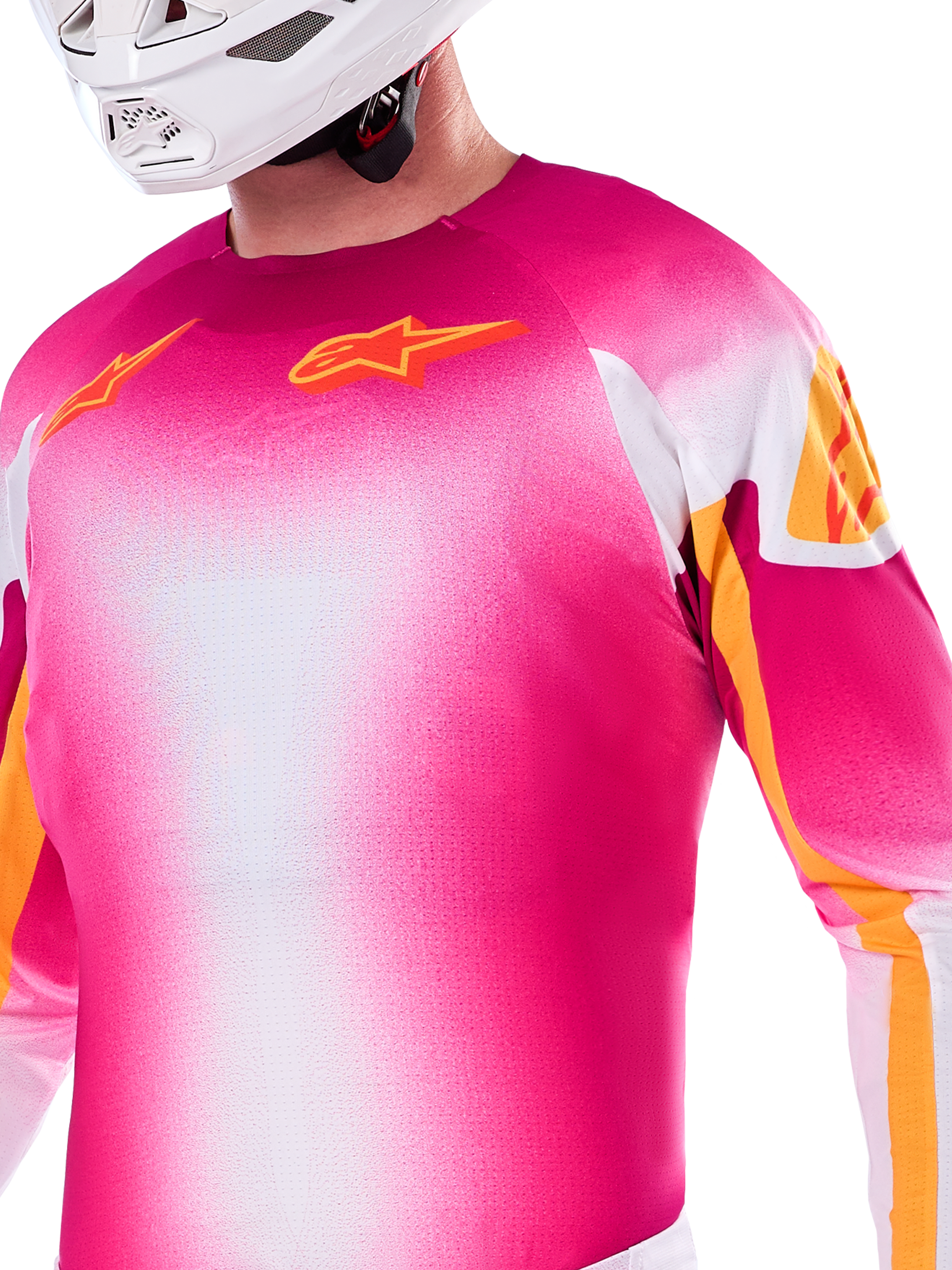 Alpinestars Limited Edition Supertech AFD MIG Jersey, maglia da motocross con sfumatura rosa fluo e bianco, loghi Astars e accenti sulle maniche arancioni, indossata da un pilota con casco bianco, vestibilità atletica da gara