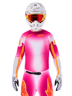 Alpinestars Maglia Limited Edition Supertech AFD MIG, maglia da motocross rosa fluo e bianca con una sfumatura vivace e loghi a stella arancioni, indossata come kit da gara completo con pantaloni coordinati, casco bianco e occhiali rossi, abbigliamento professionale per fuoristrada