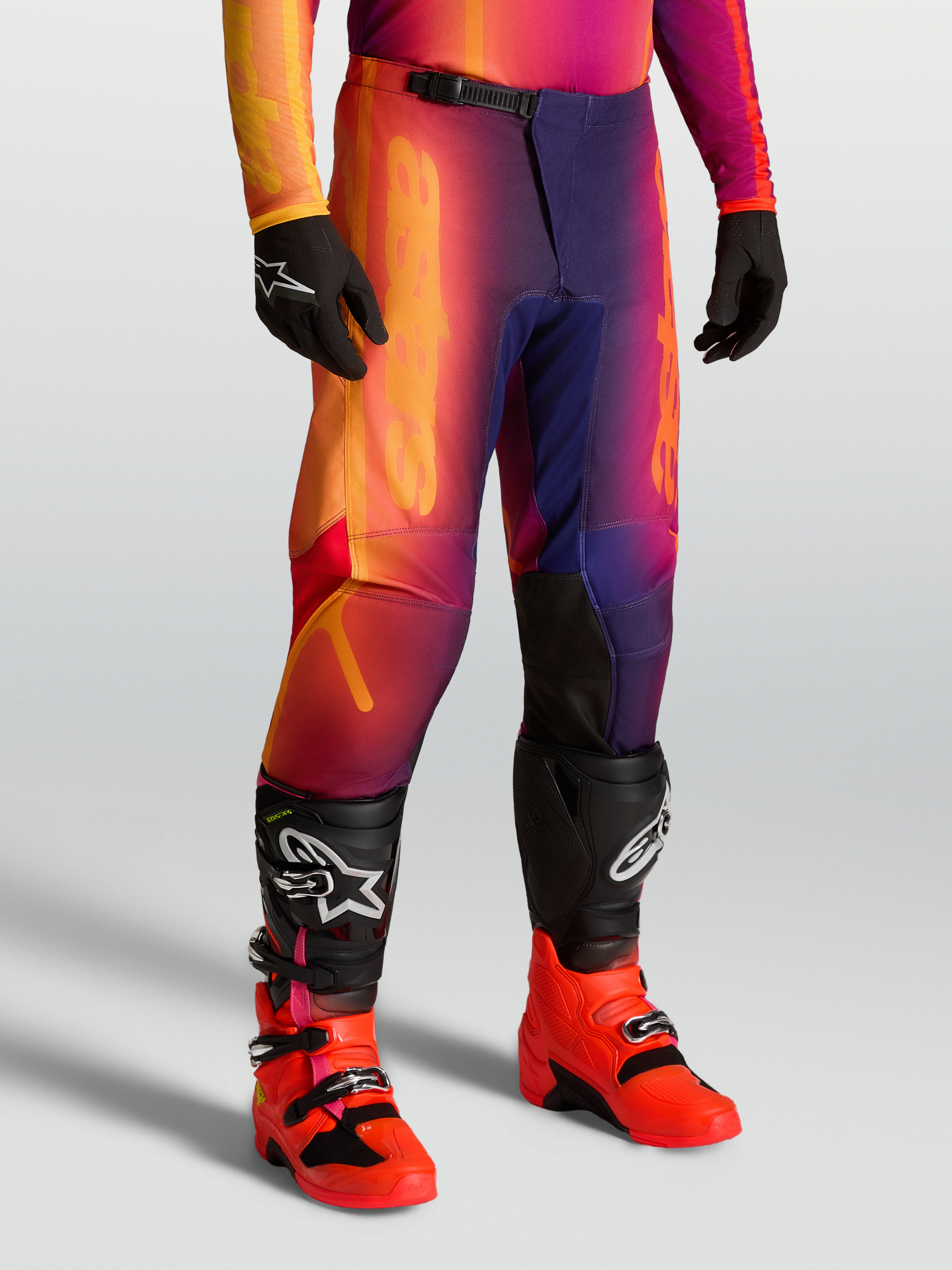 Alpinestars Pantaloni Fluid Kepler, pantaloni motocross sport-fit viola e arancione, con gambe pre-curvate e ginocchia rinforzate, indossati con stivali Tech serie.