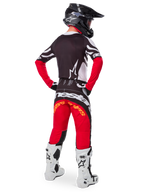 Vista posteriore di un pilota di motocross che indossa il set Limited Edition Techstar Deep Gear, con maglia nera con accenti bianchi e rossi, pantaloni rossi e neri coordinati con marchio 'Alpinestars', stivali da gara bianchi e casco nero, mostrando l'abbigliamento completo da corsa fuoristrada.