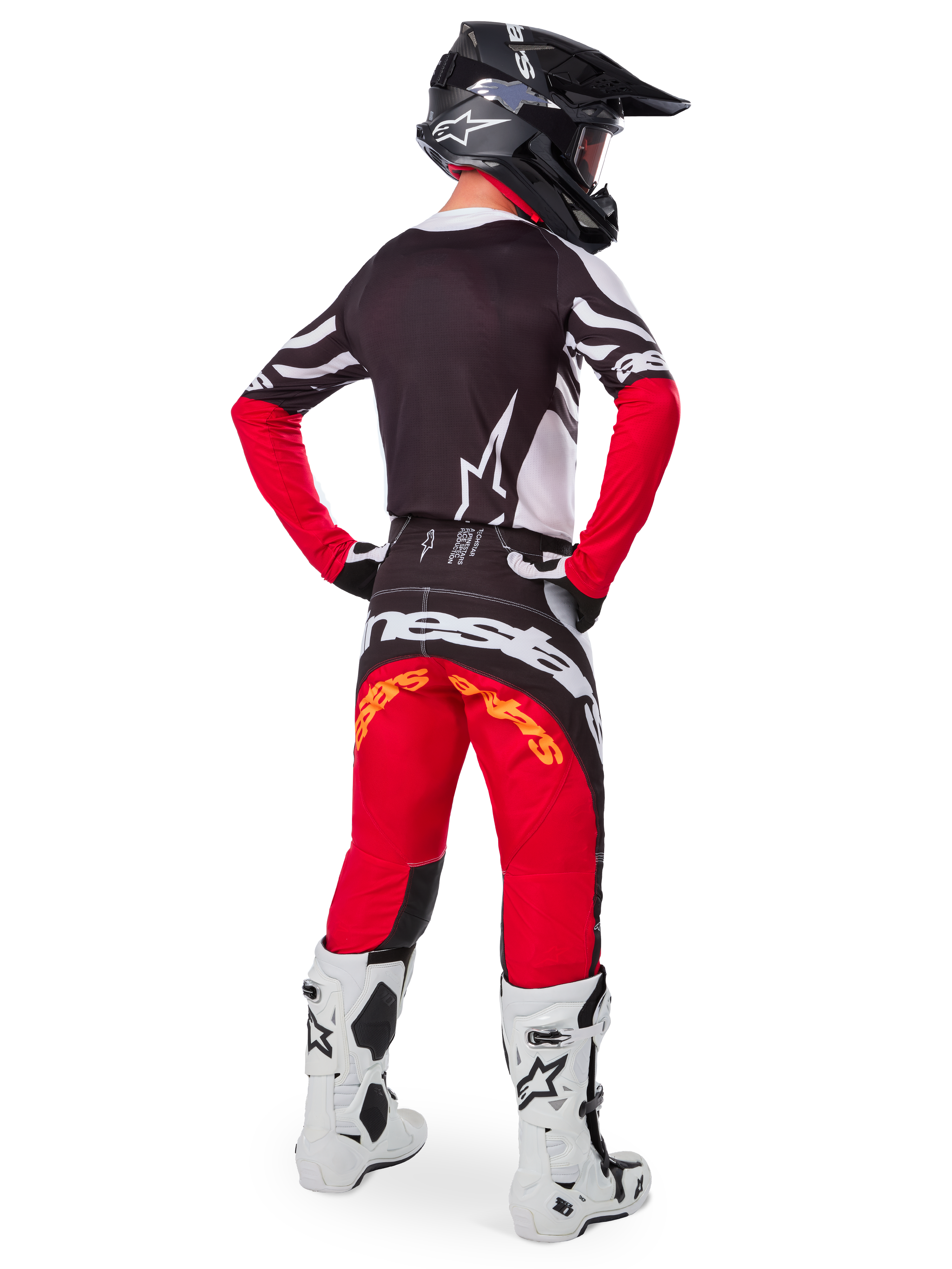 Pilota di motocross visto dal retro che indossa la maglia Alpinestars Limited Edition Techstar Deep in Black White High Red, con retro nero, logo a stella bianco e maniche rosse, abbinata a pantaloni coordinati rossi e neri, stivali bianchi e neri e casco nero per un outfit completo da gara off-road.