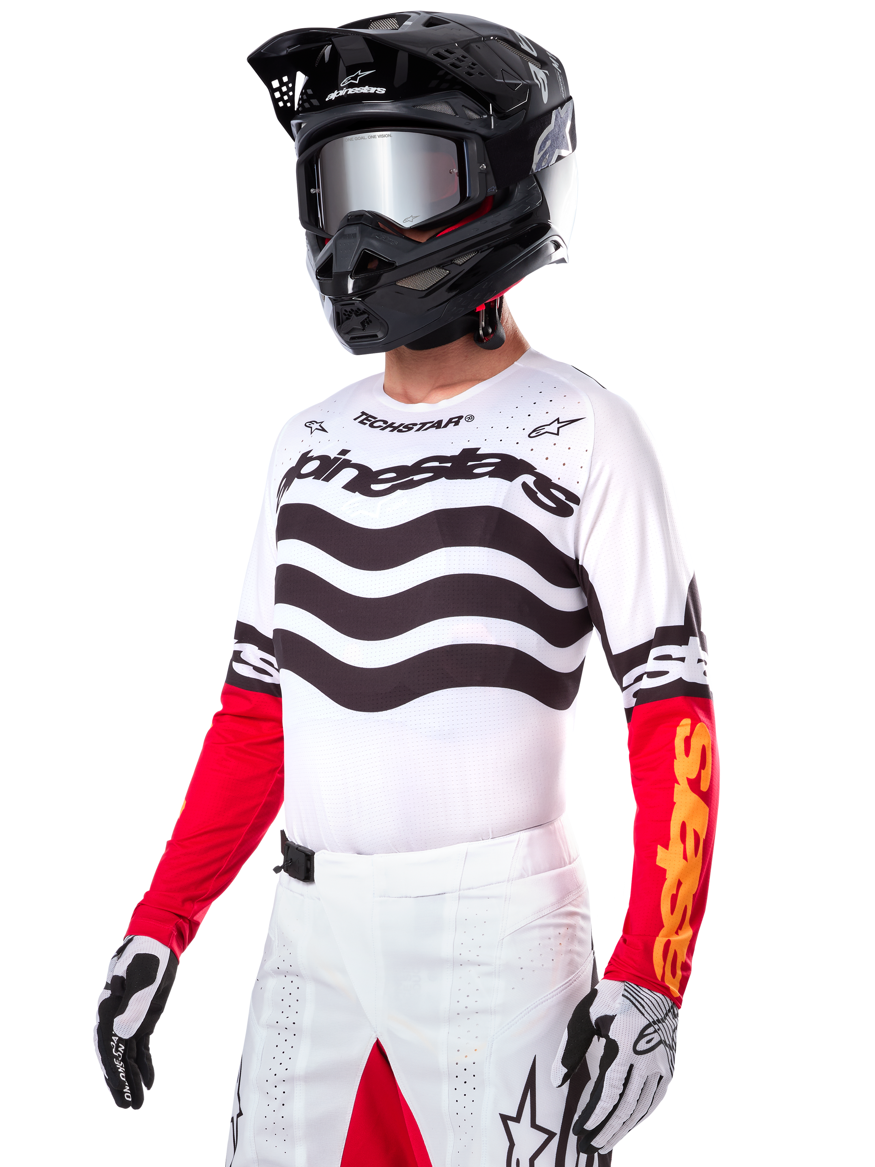 Pilota di motocross che indossa la maglia Alpinestars Limited Edition Techstar Deep, maglia bianca con strisce ondulate nere e parte inferiore delle maniche rossa, abbinata a casco nero, occhiali a specchio, guanti bianchi e neri e pantaloni da corsa bianchi, completo da motocross ad alte prestazioni.
