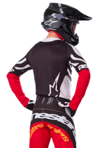 Pilota di motocross visto di spalle, maglia Alpinestars Limited Edition Techstar Deep, nero, bianco e rosso acceso, con pantaloni da gara coordinati e casco nero, vestibilità atletica per prestazioni fuoristrada
