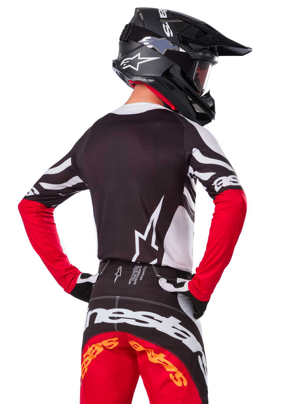 Pilota di motocross con abbigliamento completo da gara, maglia Alpinestars Limited Edition Techstar Deep in nero, bianco e rosso acceso, vista posteriore, pantaloni Techstar Deep coordinati, casco nero con maschera, guanti bianchi e neri, completo professionale per fuoristrada