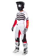 Pilota di motocross con abbigliamento da gara completo, Maglia Limited Edition Techstar Deep con strisce ondulate bianche e nere e maniche rosse, pantaloni coordinati bianchi e rossi, casco nero, stivali bianchi e neri, outfit coordinato per corse fuoristrada