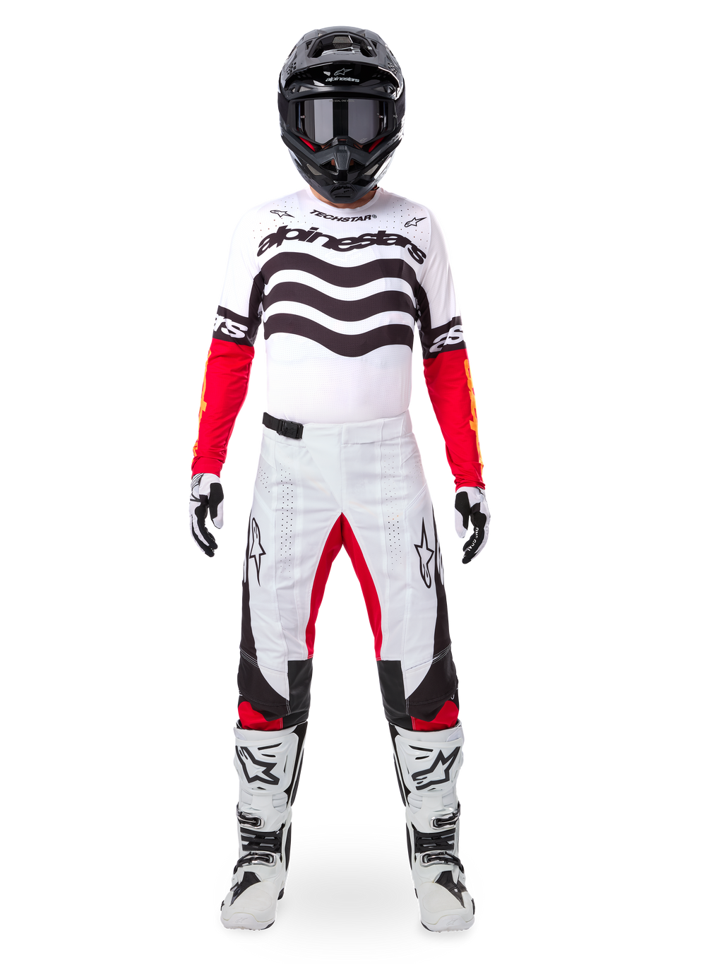 Pilota di motocross con set completo Alpinestars Limited Edition Techstar Deep, maglia bianca con grafiche a onde nere e maniche rosse, pantaloni coordinati bianchi e neri con accenti rossi, casco nero con occhiali scuri e stivali bianchi, abbigliamento professionale da gara fuoristrada