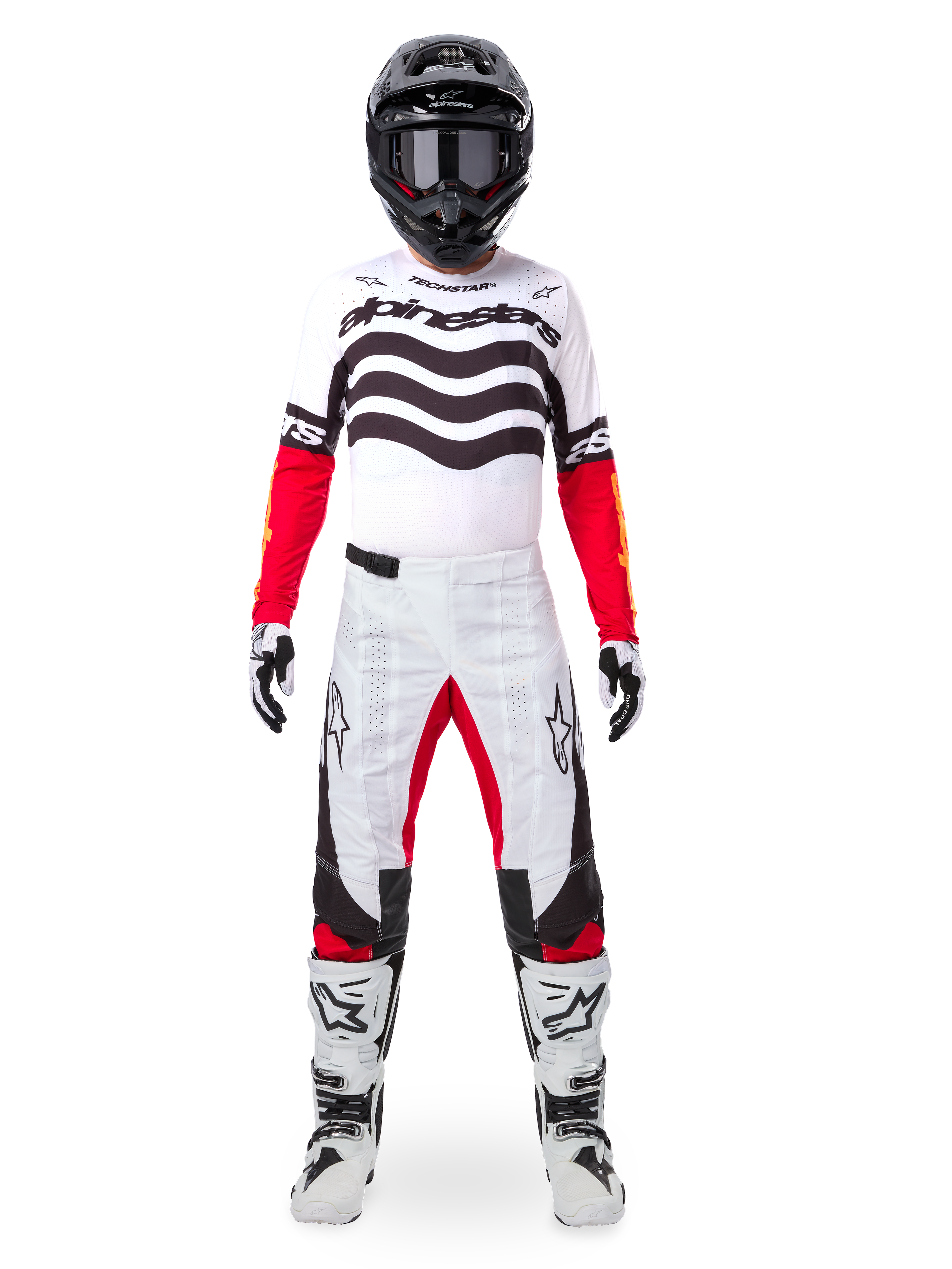 Pilota di motocross con set completo Alpinestars Limited Edition Techstar Deep, maglia bianca con grafiche a onde nere e maniche rosse, pantaloni coordinati bianchi e neri con accenti rossi, casco nero con occhiali scuri e stivali bianchi, abbigliamento professionale da gara fuoristrada