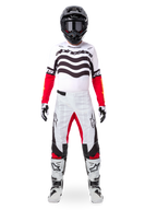 Pilota di motocross con maglia Alpinestars Limited Edition Techstar Deep, bianco, nero e rosso con grafica ondulata sul petto, pantaloni coordinati bianchi e rossi, casco nero e stivali bianchi, abbigliamento professionale completo da fuoristrada.