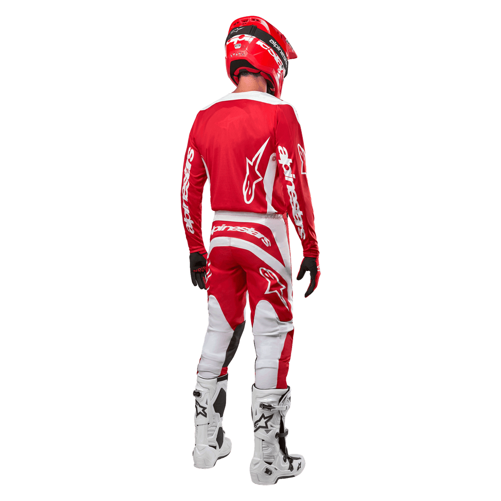 Vista posteriore di un pilota di motocross che indossa la maglia Alpinestars Fluid Lurv 2024 in Mars Red White, abbinata a pantaloni coordinati rossi e bianchi, stivali off-road bianchi e un casco rosso, mostrando il design posteriore della maglia e il marchio Alpinestars.
