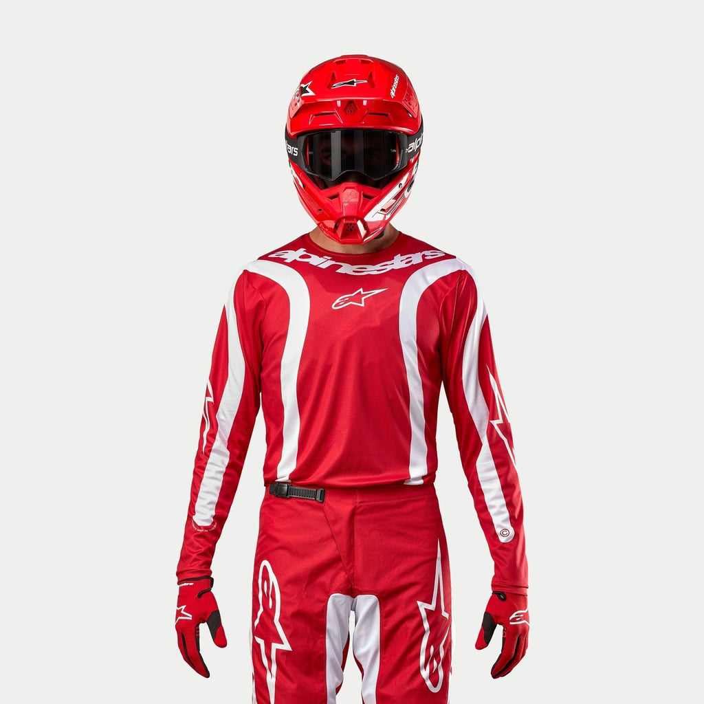 Alpinestars 2024 Fluid Lurv Jersey, maglia da motocross, rosso Marte e bianco, indossata con pantaloni, casco e guanti coordinati, con accenti grafici bianchi sulle maniche e logo evidente sul petto, vestibilità atletica per corse fuoristrada