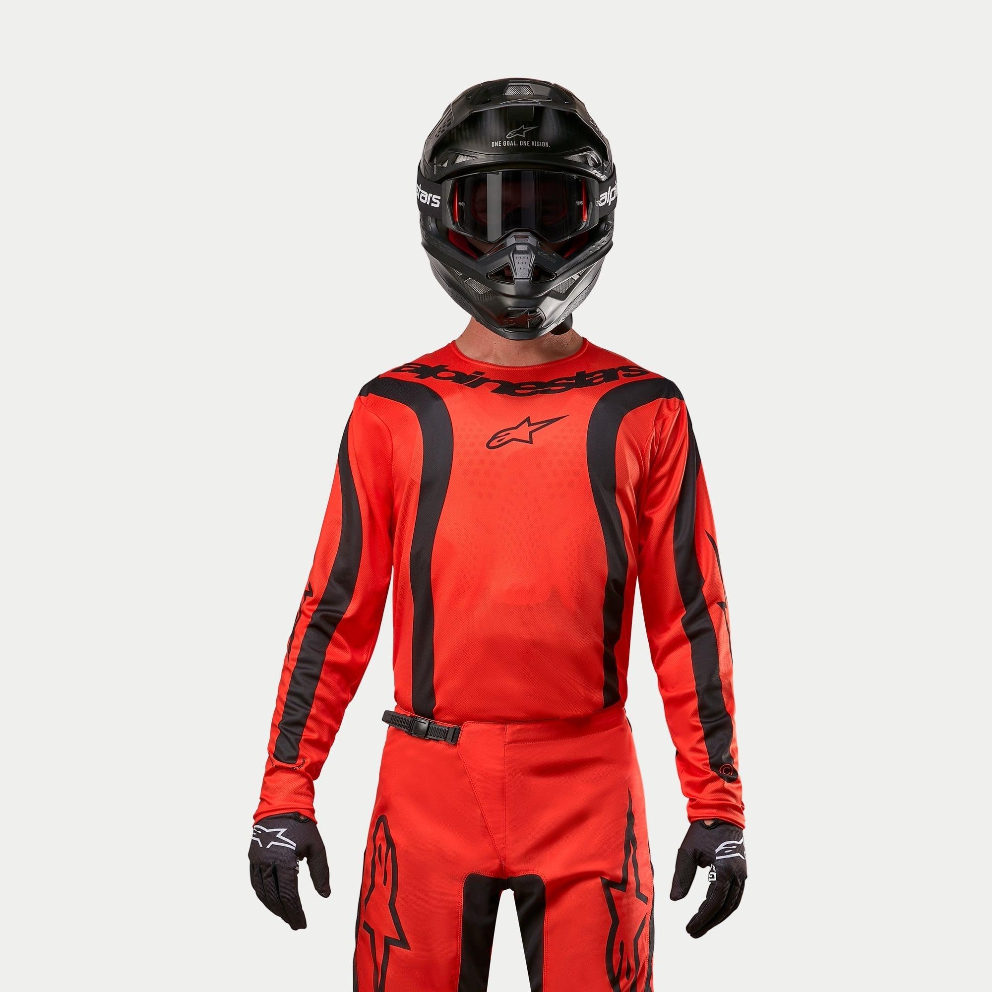 Pilota di motocross che indossa la maglia Alpinestars Fluid Lurv 2024, arancione acceso e nero, pantaloni da motocross coordinati, casco nero con occhiali e guanti neri, equipaggiamento coordinato per corse fuoristrada