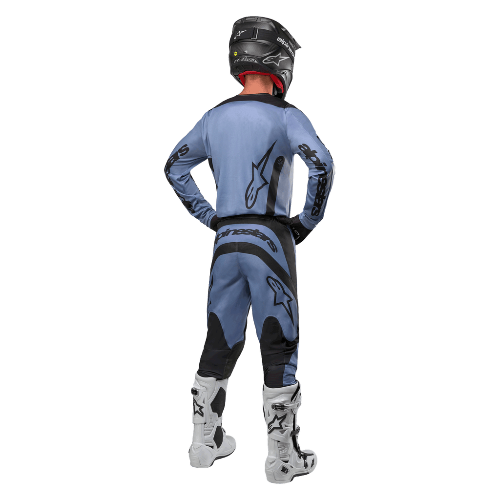 Pilota di motocross visto da dietro che indossa la maglia Alpinestars Fluid Lurv 2024 e i pantaloni coordinati in azzurro e nero, con branding nero sul retro e sulle maniche, abbinati a un casco nero e stivali bianchi.