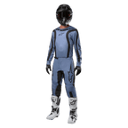 Pilota di motocross con abbigliamento completo da gara, maglia Alpinestars Fluid Lurv 2024 in azzurro e nero, pantaloni coordinati azzurri con inserti neri, stivali bianchi e neri, guanti neri e casco nero con maschera, outfit coordinato per gare fuoristrada