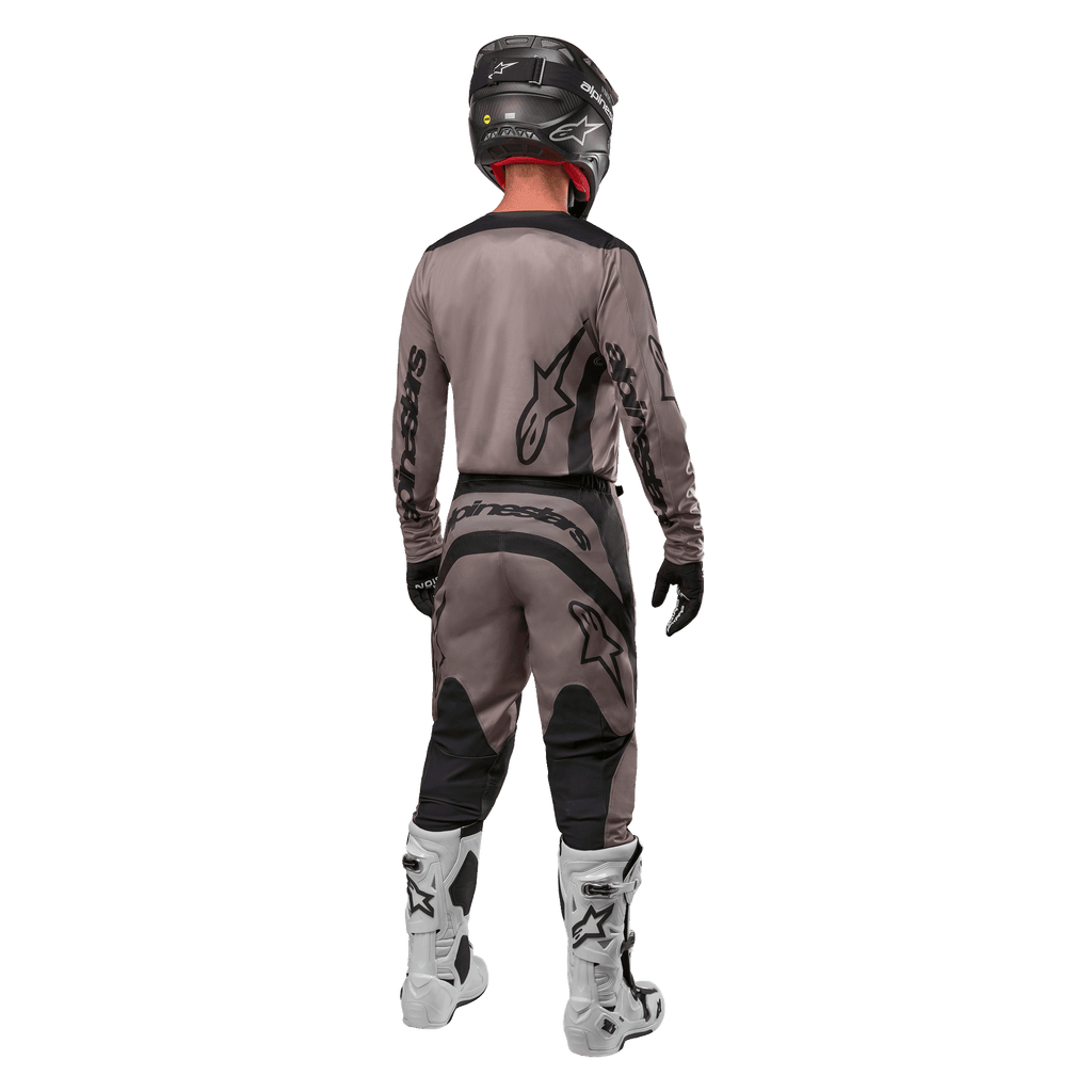 Alpinestars 2024 Fluid Lurv Jersey, maglia da motocross, Mud Black, vista posteriore di un pilota di motocross che indossa un completo da gara coordinato, casco nero e stivali bianchi, con grandi loghi Alpinestars neri e vestibilità atletica per prestazioni off-road.