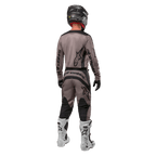 Alpinestars 2024 Fluid Lurv Jersey, maglia da motocross, Mud Black, vista posteriore di un pilota di motocross che indossa un completo da gara coordinato, casco nero e stivali bianchi, con grandi loghi Alpinestars neri e vestibilità atletica per prestazioni off-road.