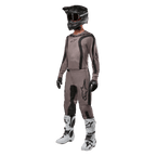 Pilota di motocross con abbigliamento da gara completo, maglia Alpinestars Fluid Lurv 2024 in Mud Black, pantaloni coordinati, casco nero con occhiali, stivali bianchi e neri e guanti neri, completo coordinato per corse off-road
