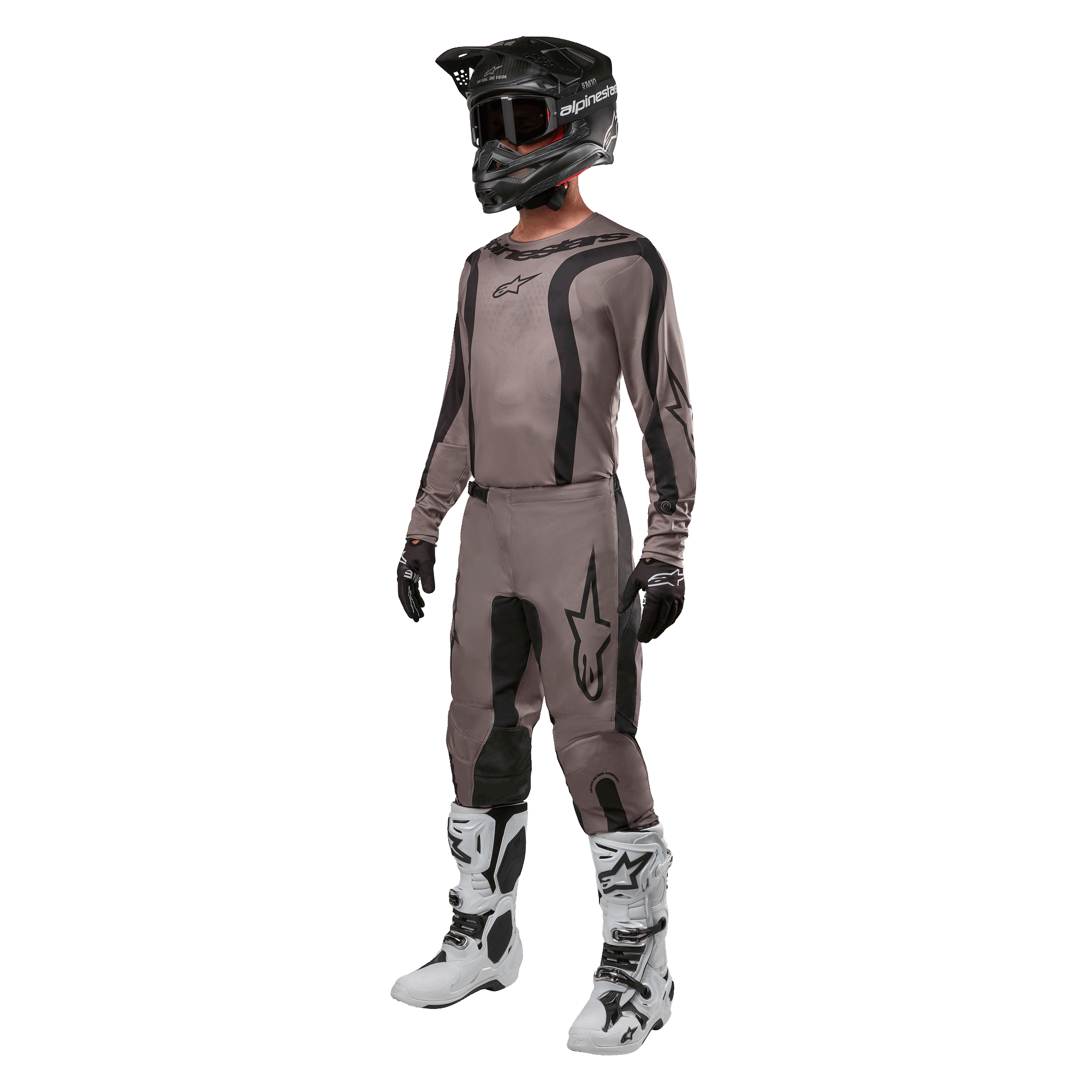 Pilota di motocross con abbigliamento da gara completo, maglia Alpinestars Fluid Lurv 2024 in Mud Black, pantaloni coordinati, casco nero con occhiali, stivali bianchi e neri e guanti neri, completo coordinato per corse off-road