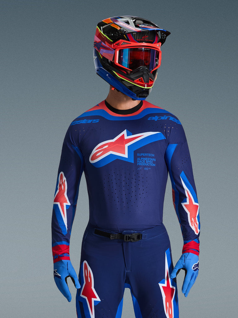 Alpinestars Supertech Vista Jersey 2026, maglia da motocross, Dark Navy, Hot Coral e Cobalt, indossata con pantaloni coordinati e casco, con grande logo a stella sul petto e branding race spec, vestibilità atletica con pannelli in mesh ventilati per prestazioni racing d'élite
