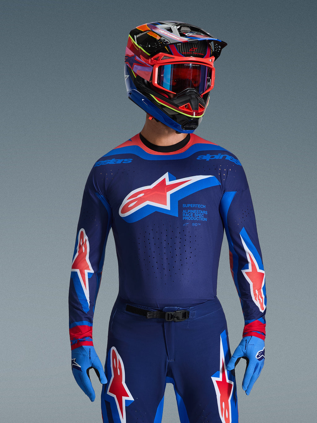 Alpinestars Set Completo Supertech Vista 2026, abbigliamento professionale da motocross, maglia e pantaloni blu navy con vistosi loghi a stella rossi e bianchi, abbinato a casco da corsa multicolore, maschera rossa e guanti azzurri, completo da gara professionale coordinato