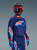 Pilota di motocross con Maglia Supertech Vista 2026 in Dark Navy, Hot Coral e Cobalt, pantaloni e guanti coordinati, casco multicolore con maschera rossa, set di abbigliamento professionale per gare fuoristrada