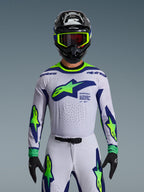 Set completo Alpinestars Supertech Vista 2026, maglia e pantaloni da motocross, bianco con grafiche blu e verde neon, indossato con casco nero e occhiali neon, con ventilazione tagliata al laser e vestibilità atletica da gara per competizioni professionistiche.