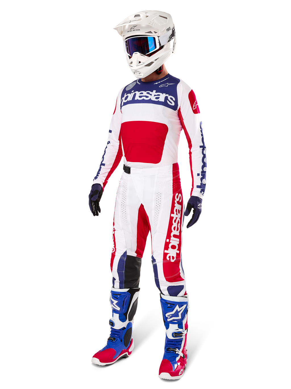 Pilota di motocross con abbigliamento completo da gara, con la maglia Alpinestars Limited Edition Techstar Fortitude in rosso acceso, bianco e blu. Pantaloni da motocross coordinati, casco bianco con occhiali blu e stivali blu e rossi, per un look coordinato ideale per competizioni off-road.