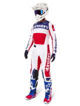 Pilota di motocross con abbigliamento completo da gara, con la maglia Alpinestars Limited Edition Techstar Fortitude in rosso acceso, bianco e blu. Pantaloni da motocross coordinati, casco bianco con occhiali blu e stivali blu e rossi, per un look coordinato ideale per competizioni off-road.
