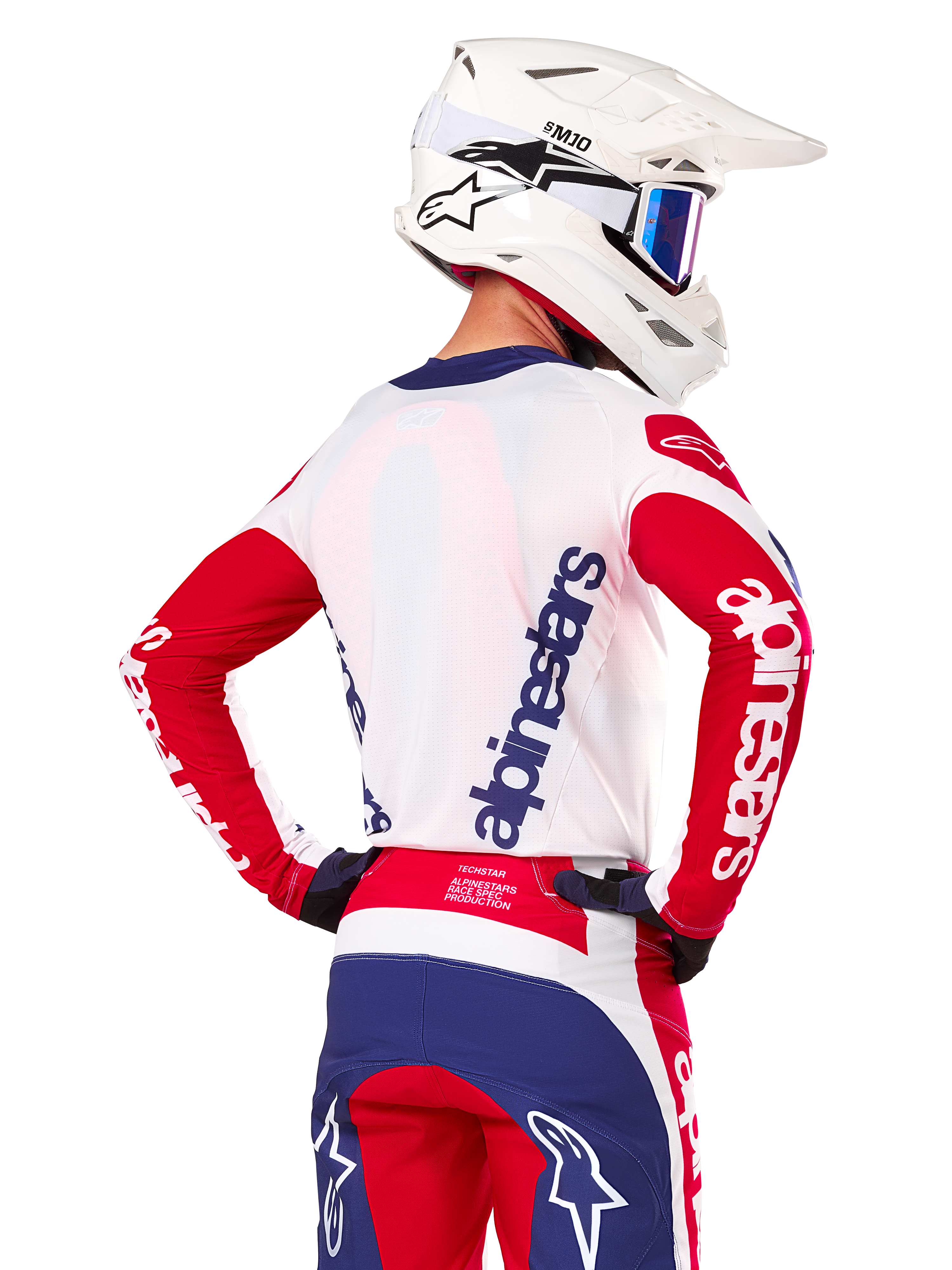 Alpinestars Limited Edition Techstar Fortitude Jersey, maglia da motocross, rosso brillante, bianco e blu, vista posteriore su un pilota con casco bianco e abbigliamento coordinato, con loghi Alpinestars evidenti su schiena e maniche, progettata per gare fuoristrada ad alte prestazioni.